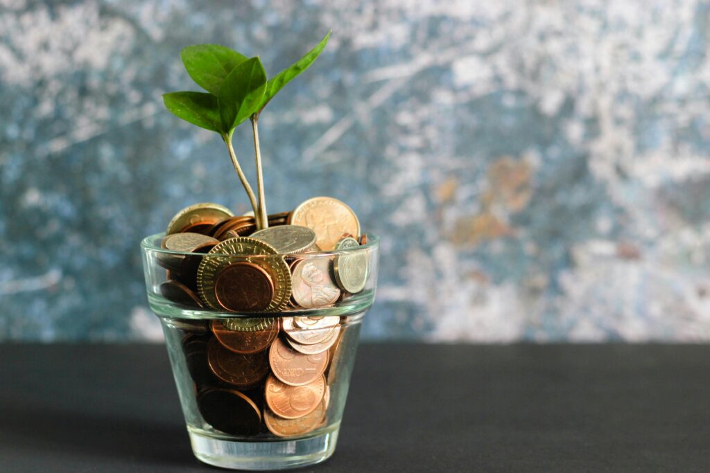 a glass filled with coin and a small plant it showing money is growing